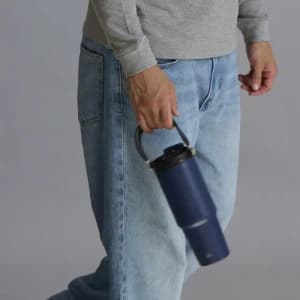 A drink bottle in navy blue, featuring a handle, held by a person wearing grey and denim.