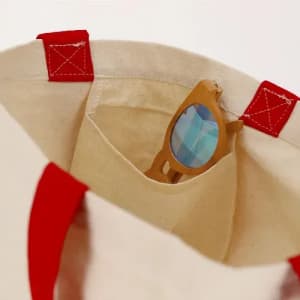 A tote bag with red handles and a beige body, featuring a pair of sunglasses nestled inside.