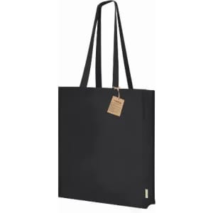 A tote bag in solid black with long handles and a tag attached. The bag features a simple, minimalistic design.