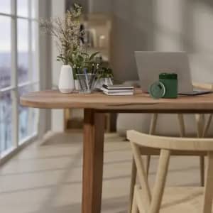 A drink bottle in green sits on a wooden table beside a laptop, plants, and stationery in a well-lit room.