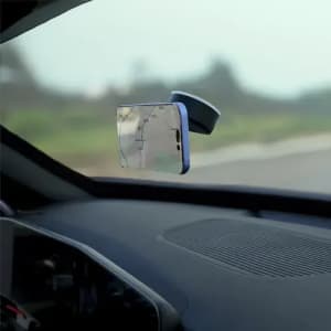 A phone mount with a sleek design, placed on a car’s windscreen, featuring a transparent holder.