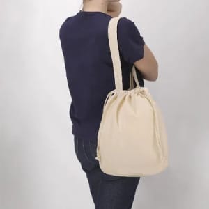 A drawstring bag in beige worn over the shoulder, featuring a cinched top and soft fabric.