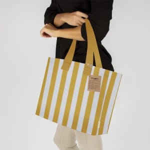 A tote bag with yellow and white stripes, featuring long handles and a tag, being held by a person.