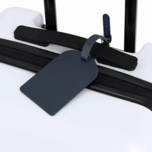 A white suitcase with a navy luggage tag attached to the handle. Features a black zipper.