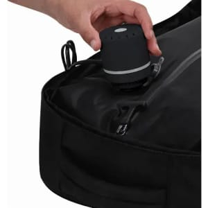 A portable speaker in black being placed on a black backpack, showcasing a compact design and sleek appearance.