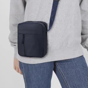 A navy crossbody bag with a zippered compartment, worn on a grey sweatshirt over jeans.
