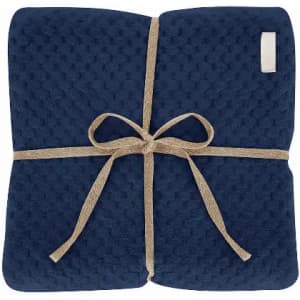 A navy throw blanket tied with a natural-coloured ribbon, featuring a textured design. It has a small logo on one corner.