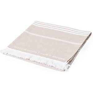 A beige cotton towel with white stripes and fringed edges, featuring a subtle logo.