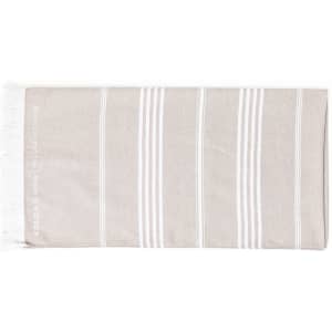 A cotton towel with a beige and white striped design, featuring tassels at one end and a logo.