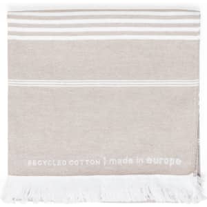 A beige towel with white stripes and fringes, made from recycled cotton, featuring a branding logo.