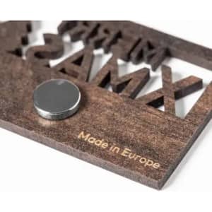 A wooden promotional item featuring raised letters and a metallic disc, with text indicating it's made in Europe.
