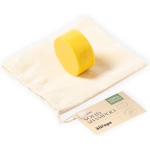 A solid shampoo bar in yellow, resting on a cream-coloured fabric bag with a tag.