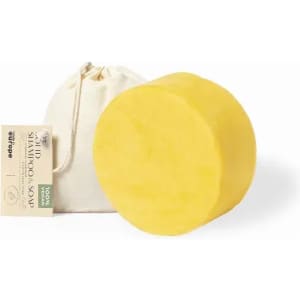 A solid shampoo bar in a circular shape, yellow in colour, accompanied by a small drawstring bag.