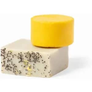 Two solid soap bars stacked, one yellow and circular on top of a rectangular bar speckled with black.