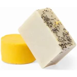Two soap bars are displayed: one is yellow and round, and the other is rectangular with a beige surface sprinkled with black seeds.