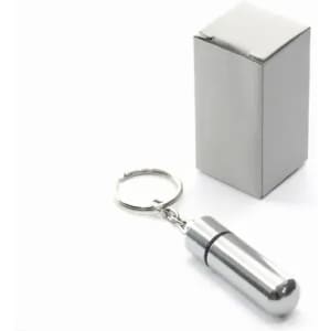 A silver keychain pill holder next to a plain white box. The pill holder has a cylindrical shape.