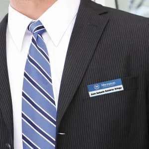 A person in a black pinstripe suit and blue striped tie, wearing a name badge with a logo.