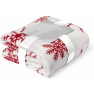 A folded blanket in white with red snowflake patterns, secured with a silver ribbon.