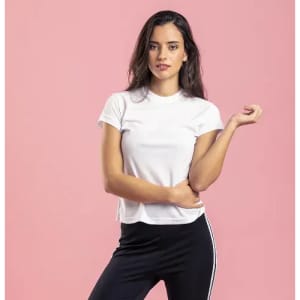 A model wearing a white t-shirt and black trousers with a stripe, posing against a pink background.