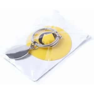 A keyring with a silver loop and a yellow circular charm, packaged in clear plastic.
