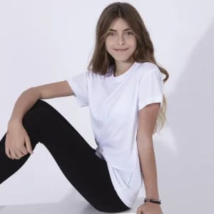 A white T-shirt is displayed, worn by a girl seated in black leggings, with long brown hair and a smile.