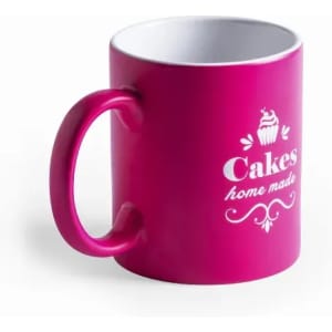 A pink mug with a white interior, featuring a cupcake design and text that reads "Cakes home made."