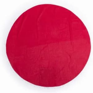 A round, red blanket or throw with a plush texture. It features a clean, simple design and is well-finished around the edges.