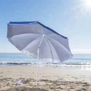 A beach umbrella with a blue trim, anchored in the sand, overlooking a sunny coastline and gentle waves.