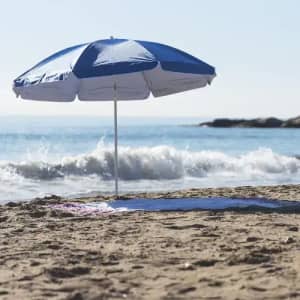 A beach umbrella featuring blue and white panels stands on sandy shores beside a gentle sea wave.