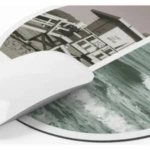 A mouse pad featuring a coastal scene with waves and a lifeguard tower in muted colours, with a smooth white edge.