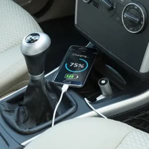 A phone charging with a visible battery percentage sits in a car's centre console next to a gear stick.