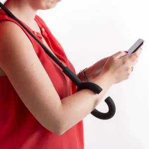 A black umbrella with a curved handle is resting on the arm of a person in a red top, who is using a smartphone.