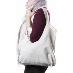 A tote bag in light beige, held by a person wearing a long-sleeve top and a scarf. The bag has no visible branding.