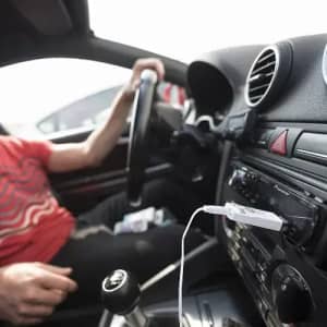 A car interior featuring a person in a red-striped shirt, with a connected USB device on the dashboard.