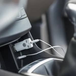 A white audio adapter plugged into a car's console, with a headphone jack connected to it.