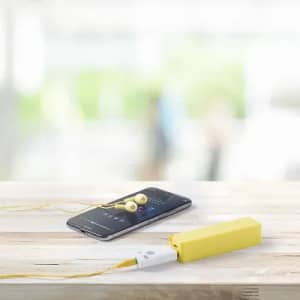 A yellow portable charger with white connectors placed next to a smartphone and yellow earphones on a wooden surface.