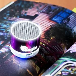 A portable speaker with a circular design, featuring a shiny purple and white exterior and a logo.