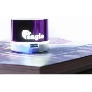 A purple portable speaker with a logo, resting on a book's cover. Light reflects off its surface.