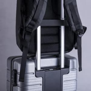 A silver suitcase with a retractable handle, featuring a black backpack secured on top with adjustable straps.
