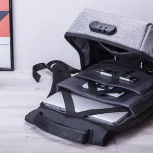 A grey backpack with a laptop compartment, pens, and a phone, laid open on a wooden surface. The bag has a logo.