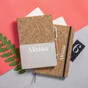 Two notebooks with cork covers, one grey and one beige, featuring a logo and placed on a colourful background.