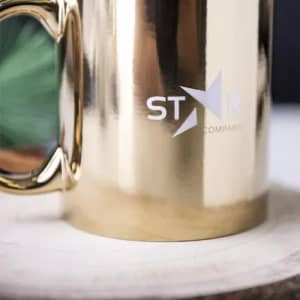 A gold drink bottle with a shiny finish and a logo on the side, set on a wooden surface.
