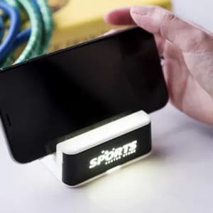A smartphone holder featuring a built-in light, with a black and white design, and a logo displayed on the front.