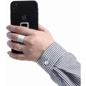 A hand holding a black smartphone, wearing a silver ring, with a striped shirt sleeve visible. The phone has a logo.