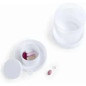 A white pill container with compartments, featuring various coloured pills inside and an additional pill outside.