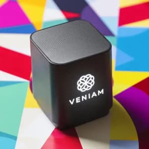 A black cube speaker with a logo on the front, sitting on a colourful geometric background.