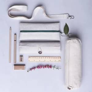 A stationery set featuring a light-coloured pouch, pencil case, wooden pencils, a ruler, a sharpener, and a plant.
