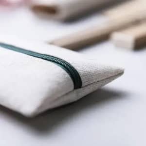 A pouch in a natural fabric with a green zipper, placed beside wooden utensils on a light background.