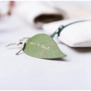 A green leaf-shaped tag with twine attached, placed on a light surface alongside a textured fabric item.