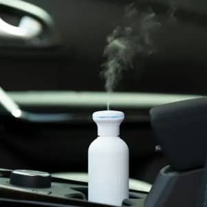 A drink bottle in white, emitting steam, positioned in a car cup holder. It has a logo.